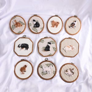 May include: A collection of framed fiber art pieces featuring various animals. The artworks include dogs, cats, and rabbits, each meticulously crafted with detailed textures and colors. The frames are wooden, and the backgrounds vary with floral and striped patterns.