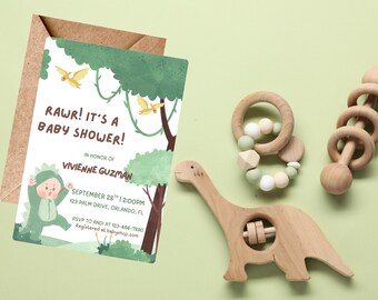 Op de afbeelding: Een uitnodiging voor een babyshower met de tekst "RAWR! IT'S A BABY SHOWER!" en een dinosaurus thema, naast houten babyspeelgoed, waaronder een dinosaurusvormige rammelaar en een ringrammelaar. De uitnodiging zit in een bruine envelop.