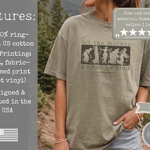 May include: A khaki-coloured short-sleeve t-shirt featuring a dark graphic print of five figures in flowing garments with the text "let the mother go out to play" and "Charlotte Mason" printed below the illustration in a dark, serif font.