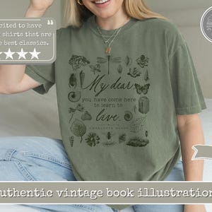 Pu&ograve; includere: Una t-shirt a maniche corte color verde muschio con una stampa grafica verde scuro. Il design include il testo "My dear you have come here to learn to live." e "Charlotte Mason" circondato da varie illustrazioni botaniche e di insetti.