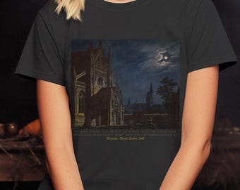 May include: Black t-shirt featuring a gothic cathedral painting under a moonlit sky. The artwork includes text from Dracula, Beam Swler, 1917. The shirt is a dark color and has a classic crew neck.