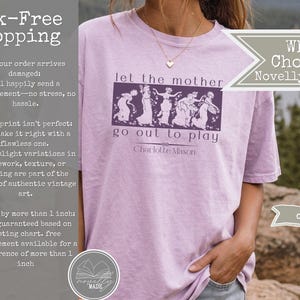 May include: A light purple t-shirt featuring a dark purple rectangular graphic with a line drawing of five figures dancing. The text reads, let the mother go out to play, followed by the name Charlotte Mason in a dark purple script font.