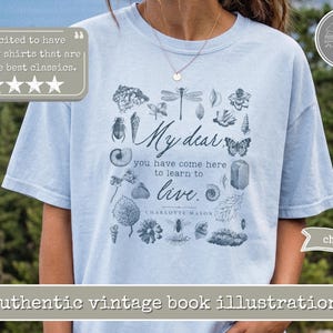 Pu&ograve; includere: Una t-shirt a maniche corte color azzurro con una stampa grafica blu scuro di varie illustrazioni naturalistiche, tra cui insetti, conchiglie e foglie. Il testo recita, My dear, you have come here to learn to live. Charlotte Mason.