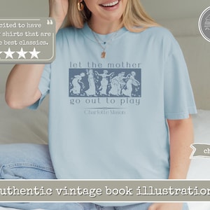 May include: A light blue t-shirt featuring a dark blue rectangular graphic with a vintage-style illustration of five figures dancing. The text reads: let the mother go out to play, followed by the name Charlotte Mason in a simple serif font.