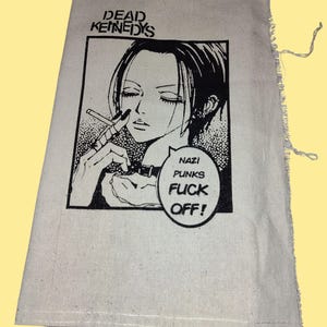 Puede incluir: Bolso tote de lona color crema con una ilustración en blanco y negro de estilo manga de una persona fumando. El texto "DEAD KENNEDYS" está encima de la ilustración, y un bocadillo dice "NAZI PUNKS FUCK OFF!"
