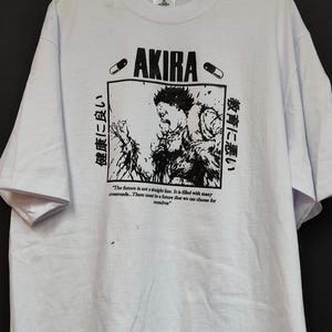 May include: White t-shirt featuring the word "AKIRA" in bold black letters, with a graphic illustration and Japanese text. The shirt also includes the quote, "The future is not a straight line..."
