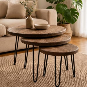 Puede incluir: Un juego de tres mesas nido redondas con tableros circulares de madera de color marrón oscuro y patas finas de metal negro en forma de horquilla. Las mesas están dispuestas en cascada, disminuyendo de tamaño desde la más grande a la más pequeña.