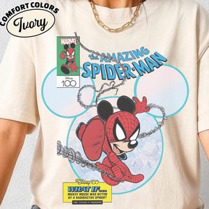 May include: Ivory Comfort Colors t-shirt featuring a comic book-style graphic. The design showcases a mashup of Spider-Man and Mickey Mouse, with the text "The Amazing Spider-Man." Additional text includes "What If..." and "100 Years of Wonder."