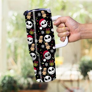 May include: A black tumbler with a white handle featuring a repeating pattern of Jack Skellington faces, Oogie Boogie figures, Santa hats, snowflakes, and wrapped gifts. The tumbler has a white handle and a black lid.