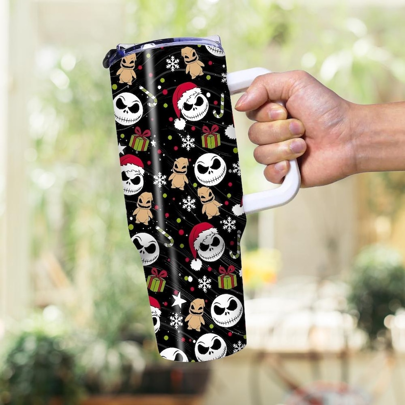 May include: A black tumbler with a white handle featuring a repeating pattern of Jack Skellington faces, Oogie Boogie figures, Santa hats, snowflakes, and wrapped gifts. The tumbler has a white handle and a black lid.