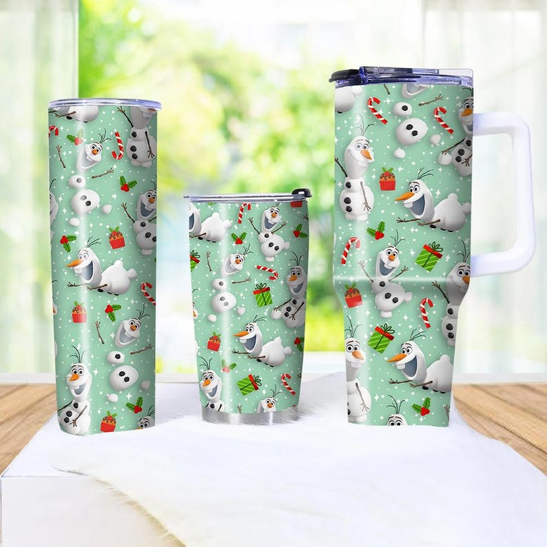 Puede incluir: Tres vasos aislados con un fondo verde menta y un patr&oacute;n repetido de Olaf el mu&ntilde;eco de nieve, bastones de caramelo y regalos envueltos. Los vasos son de diferentes tama&ntilde;os, uno de ellos con asa.
