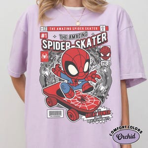 Puede incluir: Camiseta lila claro con un gr&aacute;fico de c&oacute;mic de Spider-Man en monopat&iacute;n. El dise&ntilde;o incluye las palabras "THE AMAZING SPIDER-SKATER" y "WITH GREAT POWER COMES GREAT RESPONSIBILITY". La camiseta est&aacute; etiquetada como "COMFORT COLORS Orchid".