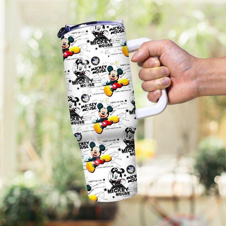 May include: White tumbler featuring a repeating pattern of Mickey Mouse illustrations in various poses, with the text "MICKEY MOUSE". The tumbler has a white handle and a black lid.