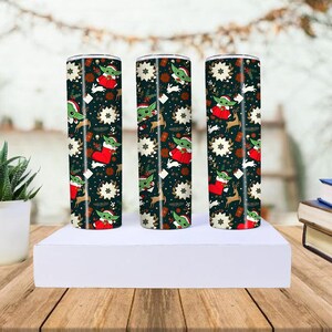 Pode incluir: Tr&ecirc;s canecas cil&iacute;ndricas de a&ccedil;o inoxid&aacute;vel com um design natalino. As canecas apresentam um fundo escuro com imagens de Baby Yoda com gorro de Papai Noel, renas, flocos de neve e meias de Natal. Elas s&atilde;o exibidas em uma plataforma branca.