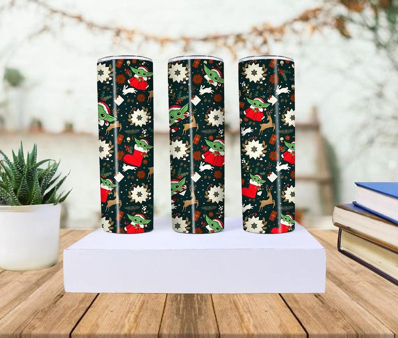 Pode incluir: Tr&ecirc;s canecas cil&iacute;ndricas de a&ccedil;o inoxid&aacute;vel com um design natalino. As canecas apresentam um fundo escuro com imagens de Baby Yoda com gorro de Papai Noel, renas, flocos de neve e meias de Natal. Elas s&atilde;o exibidas em uma plataforma branca.