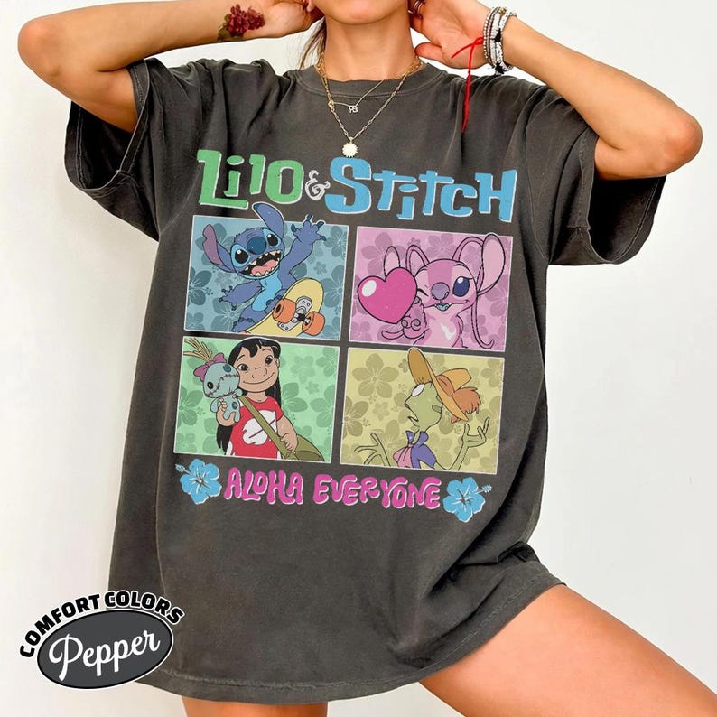May include: Dark grey t-shirt with a colourful graphic of Lilo & Stitch characters. The design includes the words "Lilo & Stitch" and "ALOHA EVERYONE". The shirt is from Comfort Colors.