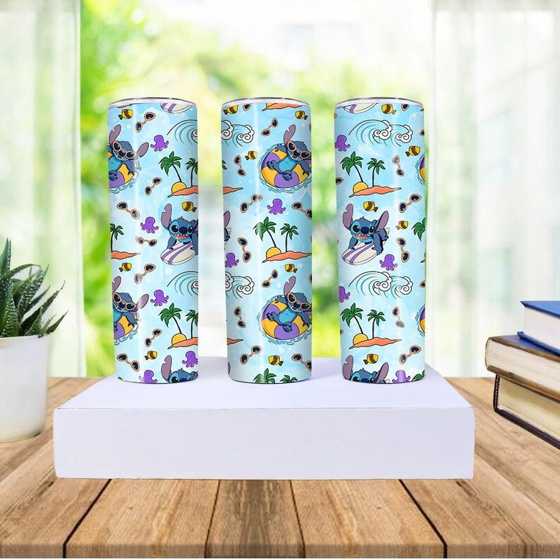 May include: Three stainless steel tumblers with a light blue background featuring a cartoon character, Stitch, surfing, floating on a tube, and wearing sunglasses. The design includes palm trees, waves, and other tropical elements.