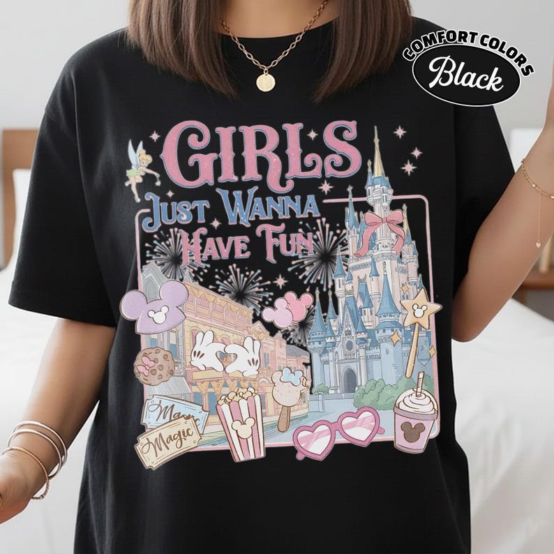 May include: Black t-shirt with a colorful graphic featuring a castle, fireworks, and the text "GIRLS JUST WANNA HAVE FUN." The design includes cartoon elements like Mickey Mouse ears, ice cream, and heart-shaped sunglasses. The shirt is labeled "Comfort Colors Black."