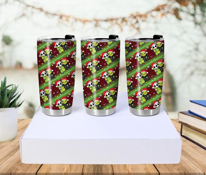 May include: Three stainless steel insulated tumblers with black lids. Each tumbler features a repeating pattern of green characters wearing Santa hats on a red background with green diagonal stripes and snowflakes.