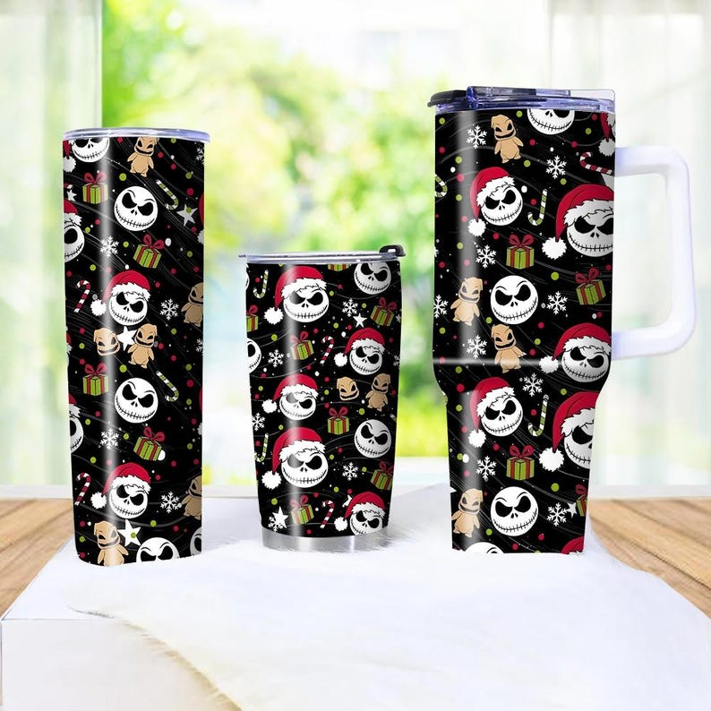 May include: Three insulated tumblers with a black background and a repeating pattern of Jack Skellington faces wearing Santa hats, gifts, snowflakes, and candy canes. The tumblers are different sizes, with one having a handle.
