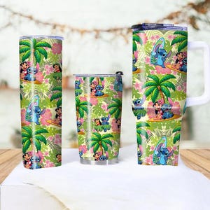 May include: A set of three insulated tumblers featuring a tropical design with palm trees, pink flowers, and cartoon characters. The tumblers include a tall, cylindrical tumbler, a shorter tumbler, and a mug with a white handle.