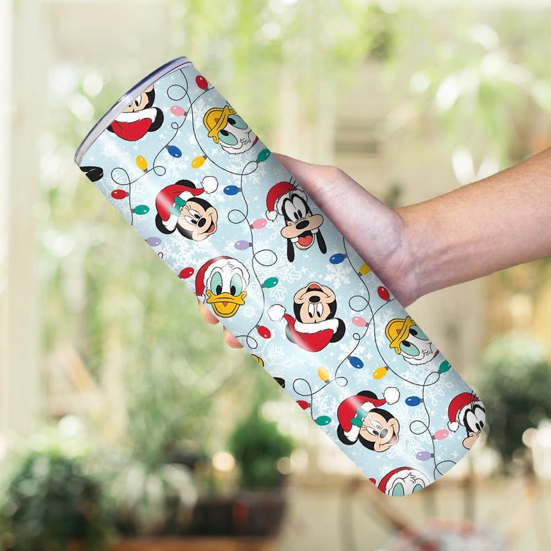 May include: A light blue tumbler featuring cartoon characters Mickey Mouse, Donald Duck, and Goofy wearing Santa hats. The tumbler is decorated with Christmas lights and snowflakes.