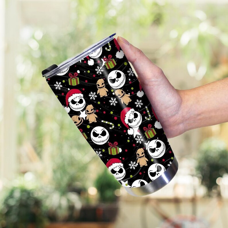 May include: A stainless steel travel mug with a black background featuring a repeating pattern of Jack Skellington faces wearing Santa hats, gingerbread men, snowflakes, and wrapped gifts. The mug has a black lid and a silver base.