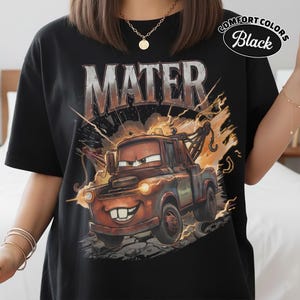 May include: Black t-shirt with a cartoon image of Mater from the film Cars. The word "MATER" is printed above the image in a metallic font. The shirt has the words "COMFORT COLORS Black" printed on the upper right.