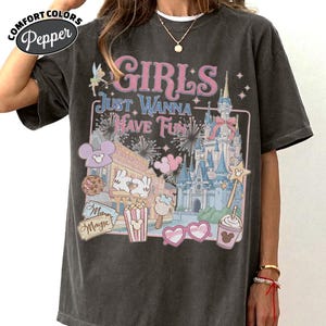 May include: Dark gray Comfort Colors t-shirt with a graphic that says "GIRLS JUST WANNA HAVE FUN." The graphic includes a castle, fireworks, and cartoon images of snacks and characters. The shirt has a relaxed fit.