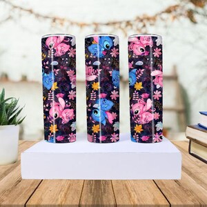 May include: Three stainless steel tumblers with a colorful design featuring the characters Stitch and Angel from Lilo & Stitch. The tumblers are decorated with a dark background, pink flowers, and yellow leaves.