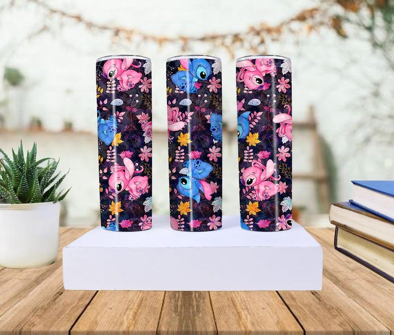 May include: Three stainless steel tumblers with a colorful design featuring the characters Stitch and Angel from Lilo & Stitch. The tumblers are decorated with a dark background, pink flowers, and yellow leaves.