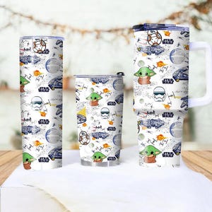 Op de afbeelding: Drie witte Star Wars-thema bekers met verschillende ontwerpen. De ontwerpen omvatten personages als Baby Yoda, BB-8 en Stormtroopers, samen met ruimteschepen en het Star Wars-logo. De bekers zijn cilindrisch en hebben een witte achtergrond.