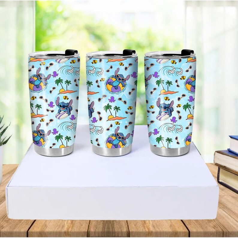 May include: Three stainless steel tumblers with black lids. Each tumbler features a light blue background with a repeating pattern of Stitch from Lilo & Stitch, palm trees, waves, and other tropical elements. The tumblers are cylindrical and have a silver base.