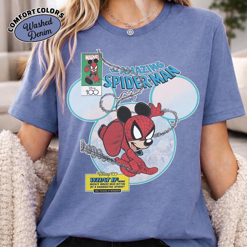 May include: A blue t-shirt featuring a graphic of Mickey Mouse as Spider-Man. The design includes the text "The Amazing Spider-Man" and "What If... Mickey Mouse Was Bitten By A Radioactive Spider?" The shirt also has the words "Comfort Colors" and "Washed Denim".
