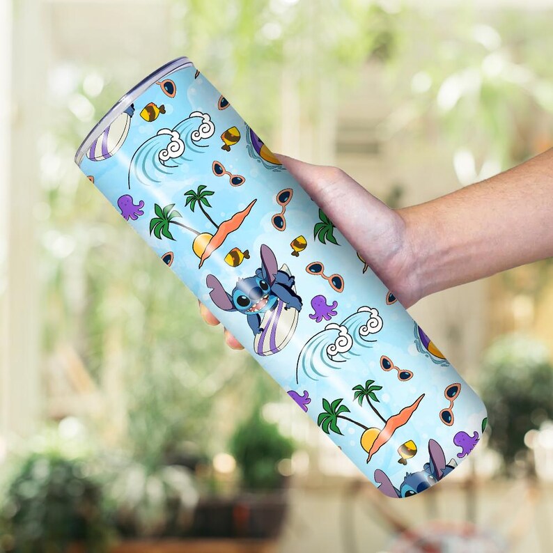 May include: A light blue tumbler featuring a tropical design with cartoon character Stitch surfing. The tumbler has a repeating pattern of waves, sunglasses, palm trees, and fish. The tumbler is held by a person.