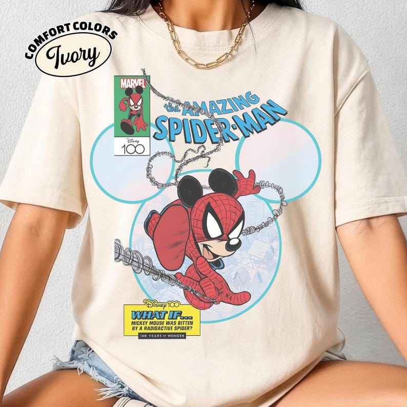 May include: Ivory Comfort Colors t-shirt featuring a comic book-style graphic. The design showcases a mashup of Spider-Man and Mickey Mouse, with the text "The Amazing Spider-Man." Additional text includes "What If..." and "100 Years of Wonder."