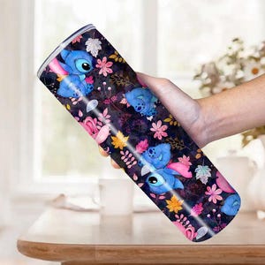 May include: A stainless steel tumbler featuring a repeating pattern of the character Stitch from Lilo & Stitch. The design includes blue Stitch figures, pink and yellow flowers, and leaves on a dark background.
