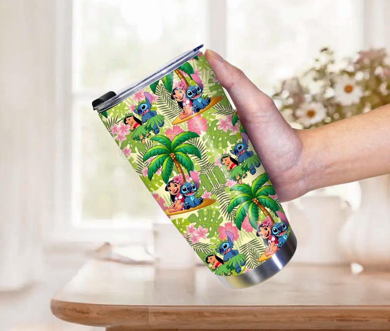 May include: A stainless steel tumbler featuring a tropical design with cartoon characters, palm trees, and pink flowers. The tumbler has a black lid and is held by a person.