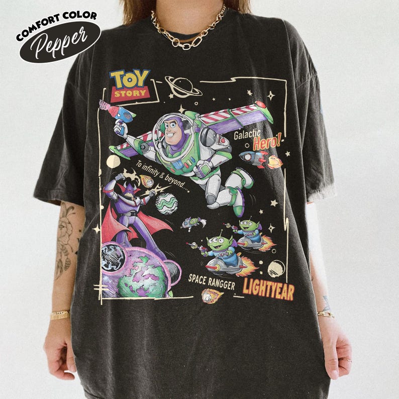 May include: A black t-shirt featuring a Toy Story graphic with Buzz Lightyear, Zurg, and aliens in space. The print includes the text Toy Story, To infinity & beyond, Galactic Hero, SPACE RANGGER, and LIGHTYEAR. The shirt has a crew neck.