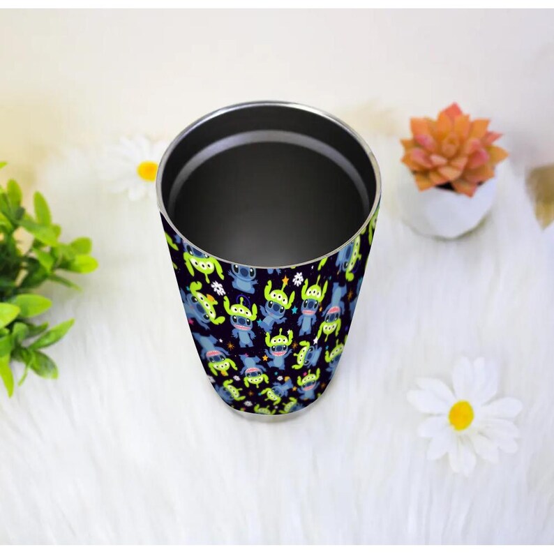 Peut inclure: Un gobelet en acier inoxydable avec un motif r&eacute;p&eacute;t&eacute; d'extraterrestres de dessins anim&eacute;s bleus et verts sur un fond bleu fonc&eacute;. Le gobelet a un bord argent&eacute; et un int&eacute;rieur noir. Le design est un th&egrave;me amusant et ludique.