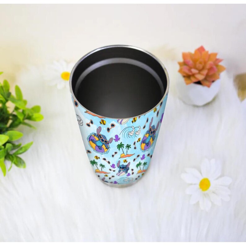 May include: A stainless steel tumbler with a blue background featuring a repeating pattern of a cartoon character in a yellow and purple floatie, palm trees, and waves. The tumbler has a silver rim and a dark interior.