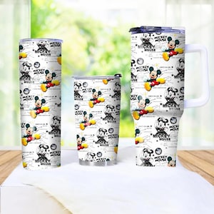 May include: Three white tumblers with a repeating pattern of Mickey Mouse illustrations and text. The tumblers vary in size, with one tall and slender, one medium, and one with a handle. The design includes Mickey Mouse in various poses.