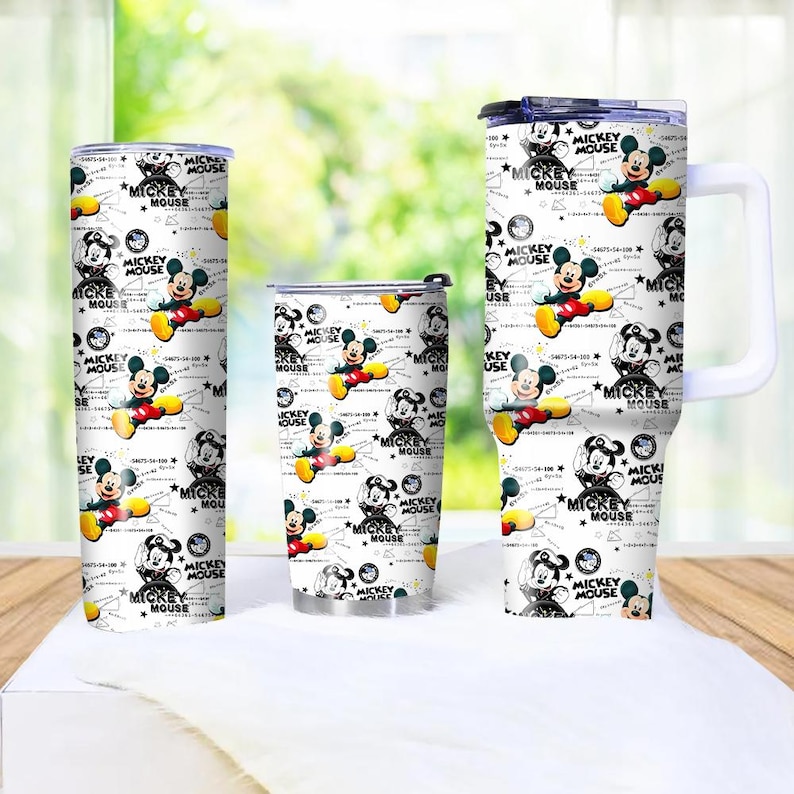 May include: Three white tumblers with a repeating pattern of Mickey Mouse illustrations and text. The tumblers vary in size, with one tall and slender, one medium, and one with a handle. The design includes Mickey Mouse in various poses.