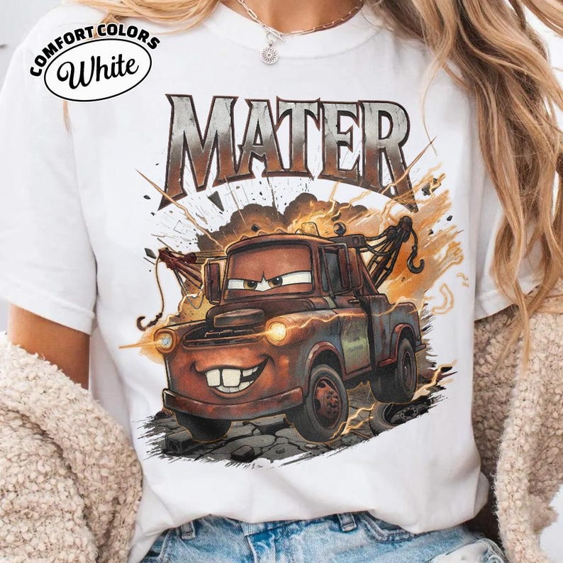 May include: White t-shirt with a graphic of Mater from the film Cars. The design includes the word "MATER" in a distressed font above the character. The shirt has the words "Comfort Colors" and "White" printed on the upper left.
