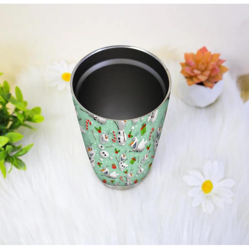 Puede incluir: Un vaso de acero inoxidable con un fondo verde menta y un patr&oacute;n repetido de mu&ntilde;ecos de nieve de dibujos animados, bastones de caramelo y regalos envueltos. El vaso tiene un interior oscuro y est&aacute; dise&ntilde;ado para bebidas.