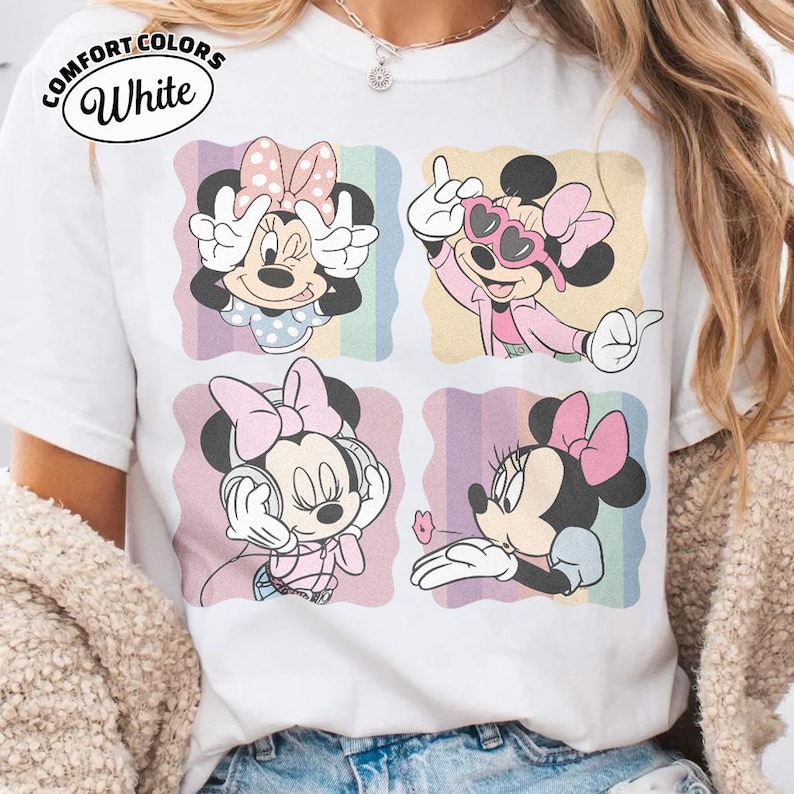 May include: White Comfort Colors t-shirt featuring four panels with Minnie Mouse illustrations. Each panel showcases Minnie in different poses, with a pink bow, against a pastel rainbow background. The shirt has the text "Comfort Colors White" in a circular design.