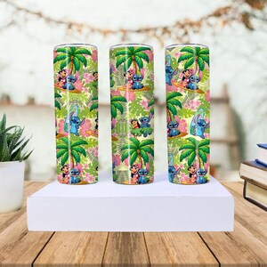May include: Three stainless steel tumblers with a tropical design featuring palm trees, flowers, and cartoon characters. The tumblers are cylindrical and decorated with a colorful pattern of green, pink, and blue.