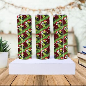 May include: Three stainless steel tumblers with a repeating pattern of green Grinch and Jack Skellington characters wearing Santa hats on a red background with white snowflakes and green diagonal stripes.
