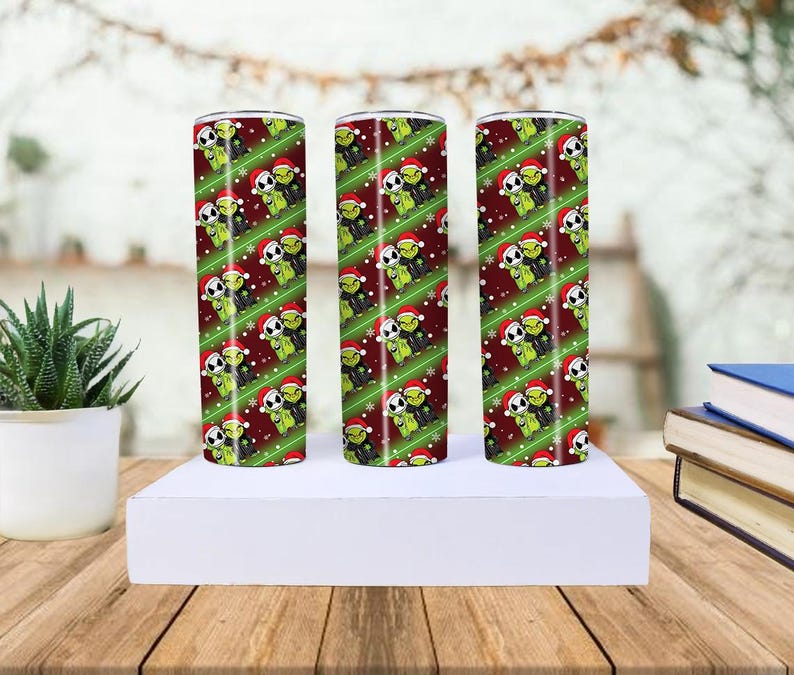 May include: Three stainless steel tumblers with a repeating pattern of green Grinch and Jack Skellington characters wearing Santa hats on a red background with white snowflakes and green diagonal stripes.