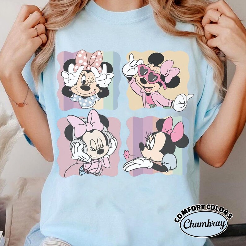 May include: Light blue t-shirt featuring four panels with Minnie Mouse illustrations. Minnie is depicted in various poses, wearing pink bows and outfits. The shirt has the text "Comfort Colors Chambray" at the bottom right.